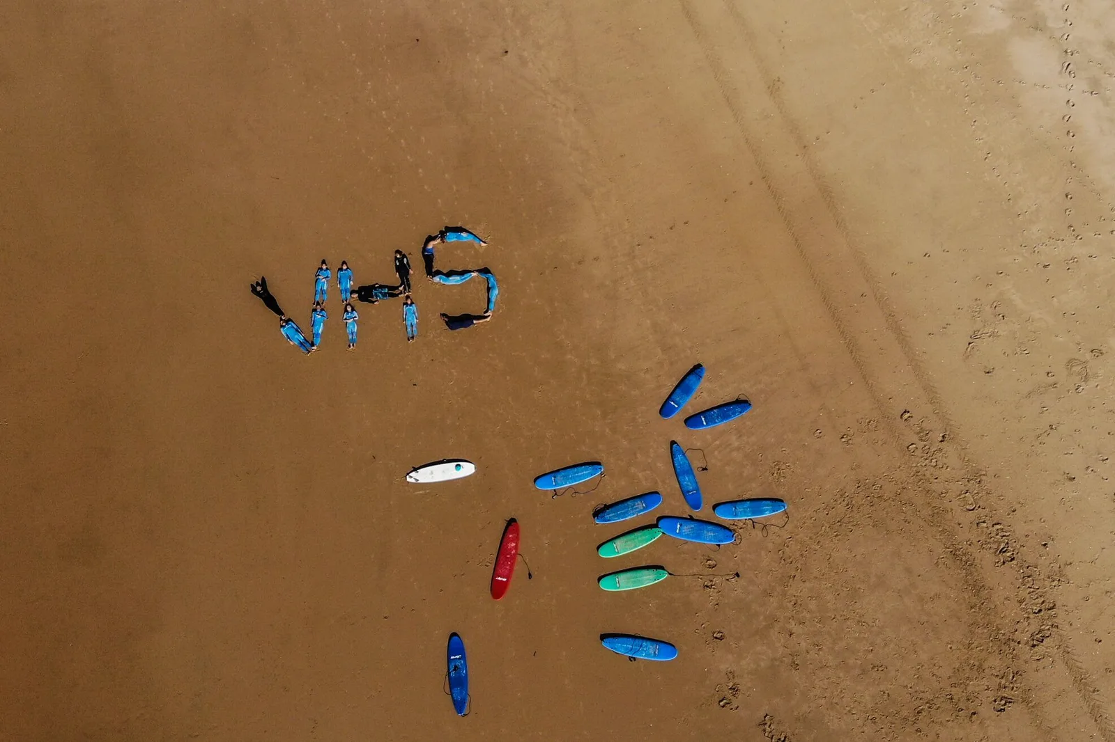Uczestnicy surf campu VHS ułożeni w znak VHS na plaży